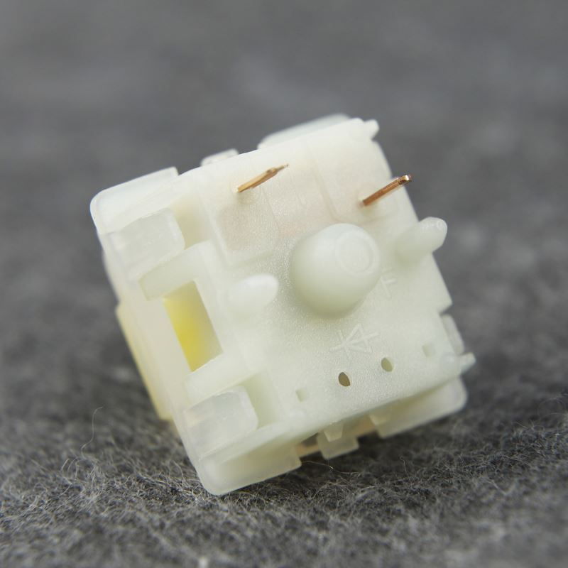 A close-up image of a single Gateron Milky Yellow Pro switch. The switch has a transparent white housing with a yellow top, and the spring is visible inside.