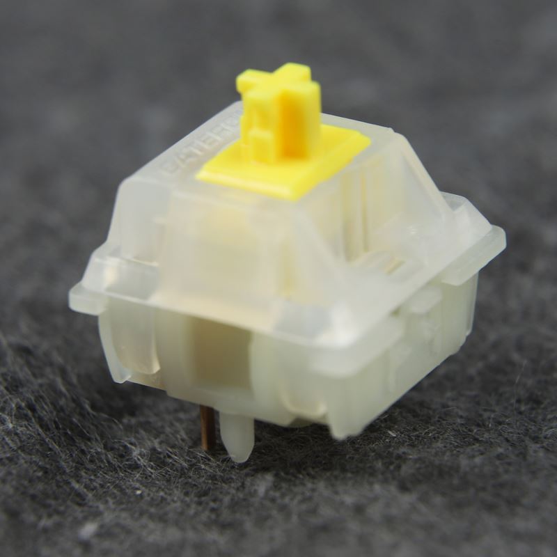 A close-up image of a disassembled Gateron Milky Yellow Pro switch. The switch has a transparent white housing with a yellow stem and spring. The housing is open, showing the internal components.