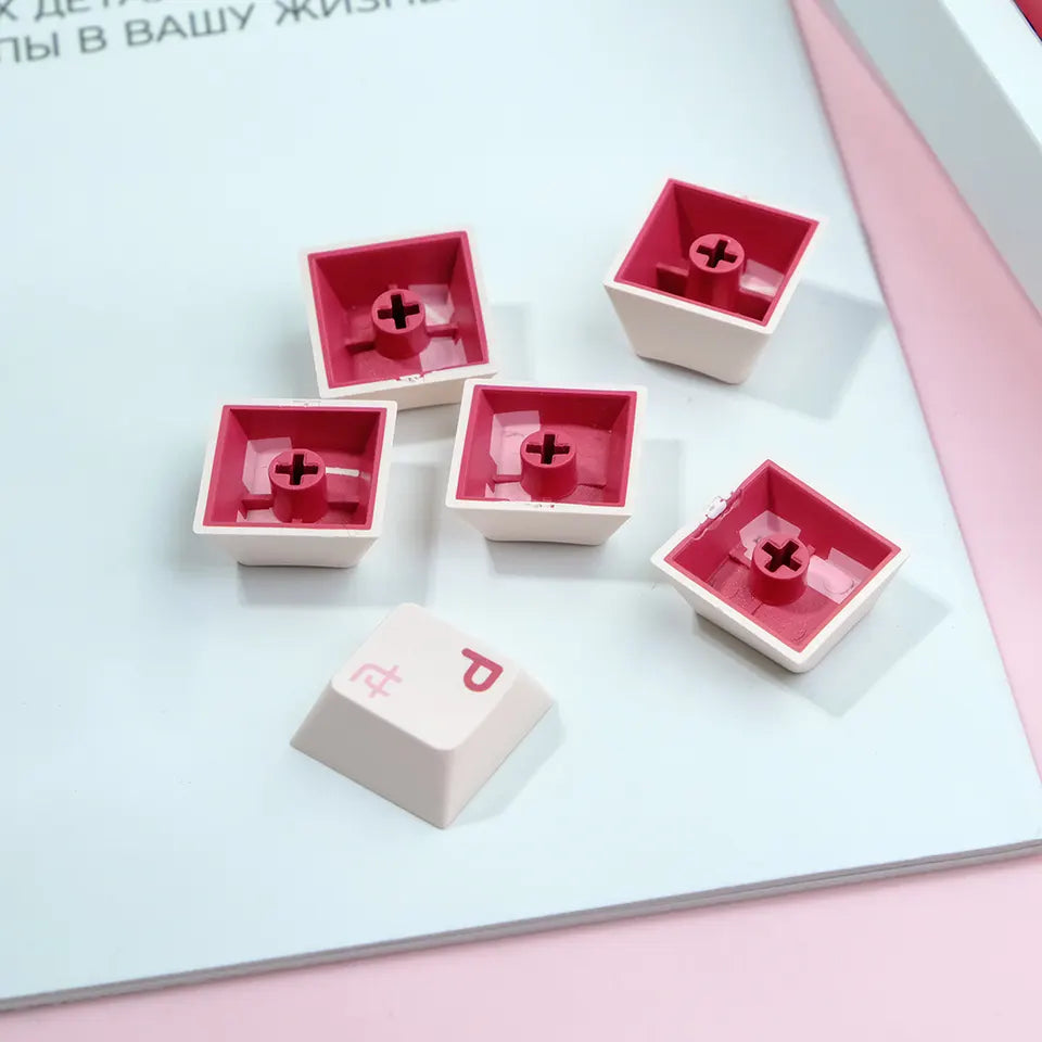 A close-up image of several pink and white keycaps arranged on a white surface. The keycaps feature a delicate rough surface and are compatible with various keyboard layouts.