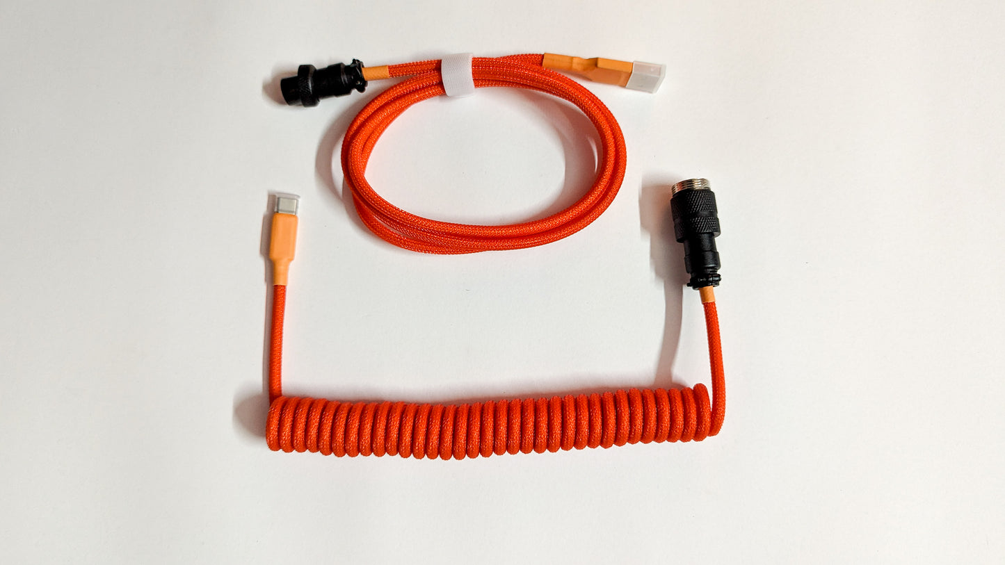 A coiled keyboard cable with orange and black connectors on both ends. The cable is orange and has a braided design.