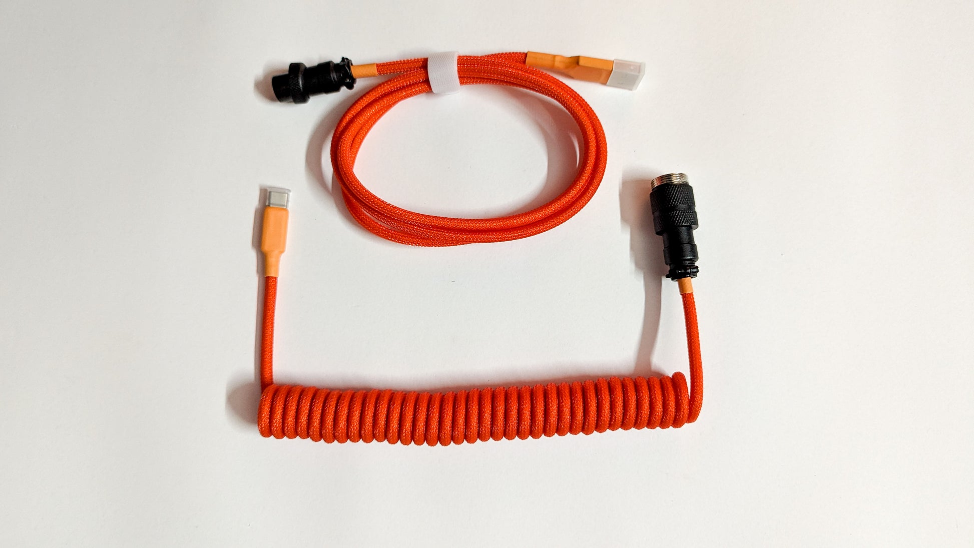 A coiled keyboard cable with orange and black connectors on both ends. The cable is orange and has a braided design.