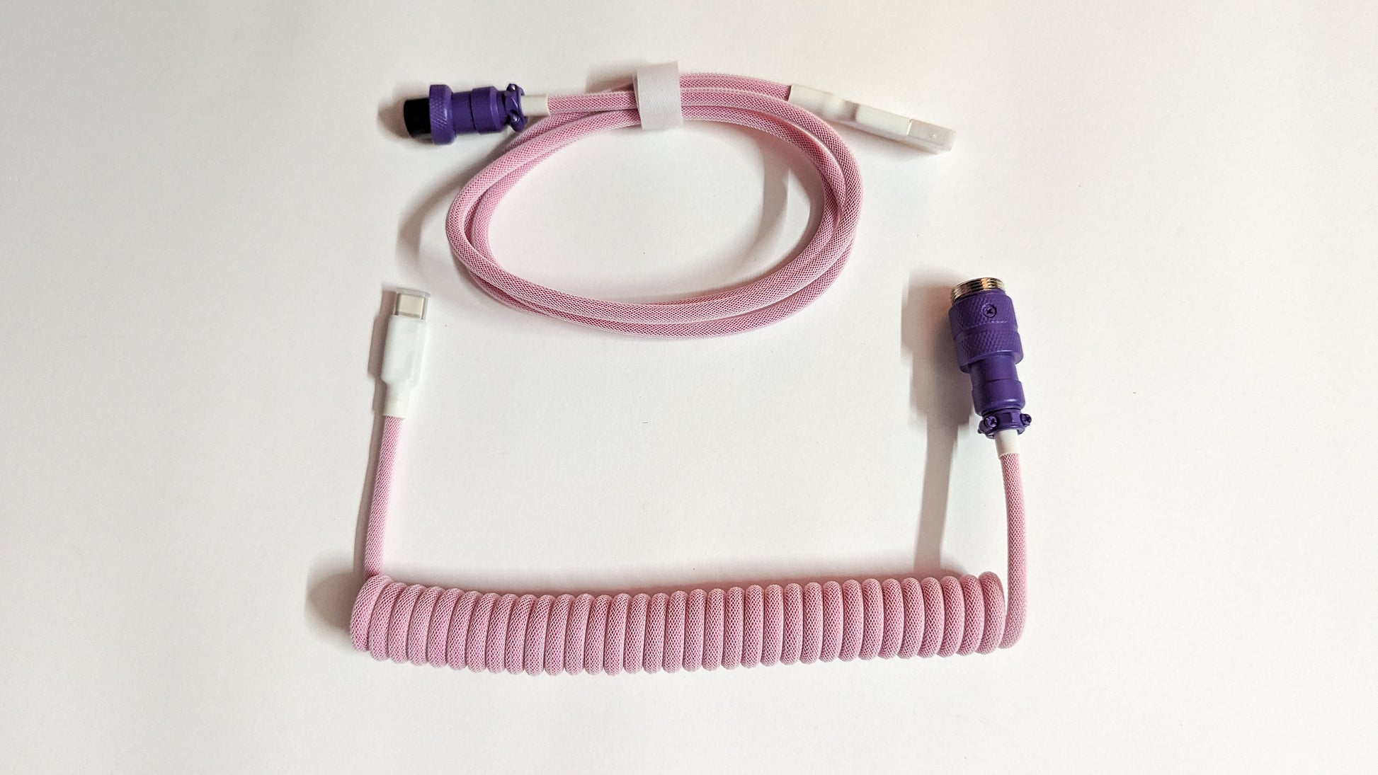 A coiled keyboard cable with a purple connector on one end and a pink connector on the other. The cable is pink and has a braided design.