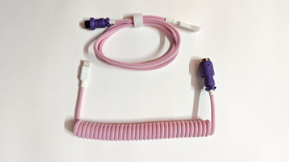 A coiled keyboard cable with a purple connector on one end and a pink connector on the other. The cable is pink and has a braided design.